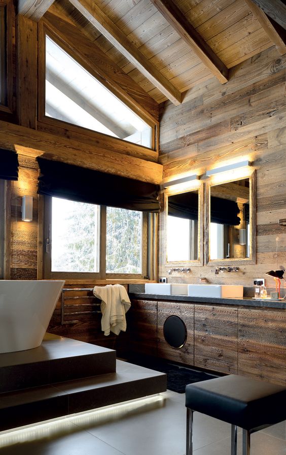 a beautiful modern chalet bathroom clad with wood all over, with a bathtub on a platform, a large wooden vanity and touches of black