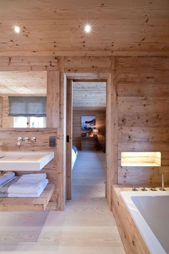 a blonde wood chalet bathroom with a floating sink and vanity, a bathtub clad with stone and a lit up niche