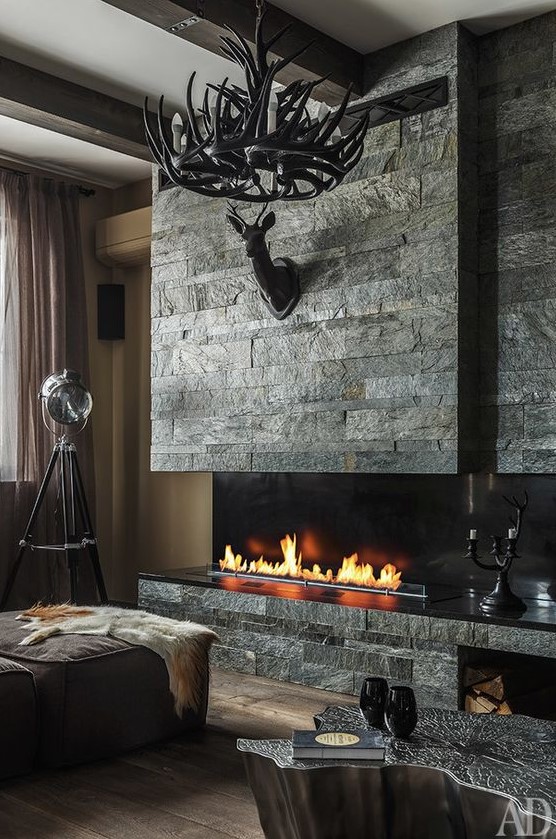 a bold refined chalet living room with neutral walls, ottomans and a catchy side table, a faux stone clad fireplace and an antler chandelier