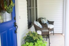 a bright summer porch with wicker furniture, shutters, a rug, potted greenery and floral pillows