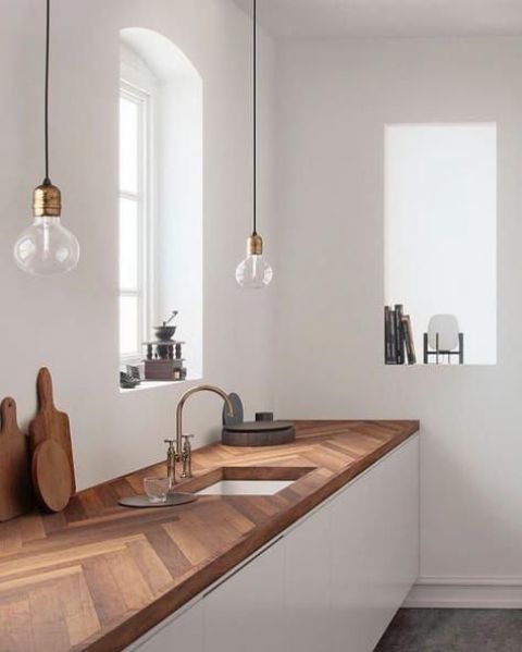 a chevron clad wooden butcher block countertop adds a textural touuch to the sleek white cabinets