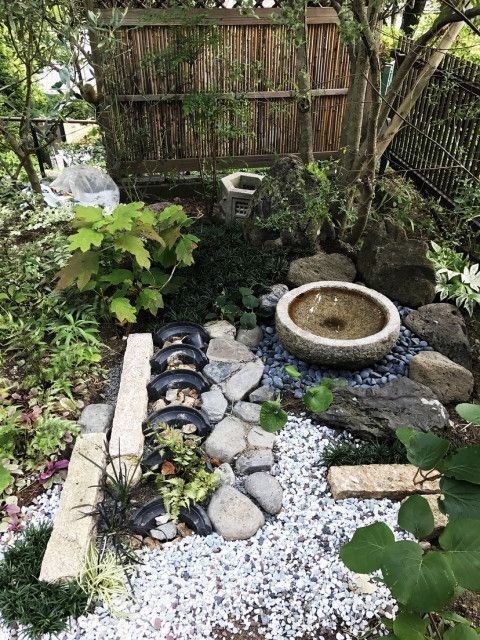 un elegante jardín japonés con guijarros, rocas, un cuenco de piedra con una fuente, árboles, vegetación y bambú