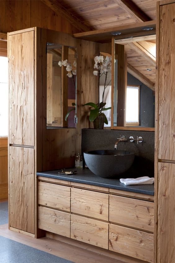 a chic chalet bathroom with plenty of textural wood, grey stone countertops, and a matching bowl sink, an orchid and a mirror