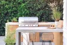 a chic contemporary bbq area of wood and concrete, with a grill and a cooking zone, a concrete dining area and rattan stools