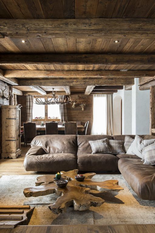a chic modern chalet living room with a stained wooden ceiling and beams, a leather sofa, a gorgeous wood slcie table