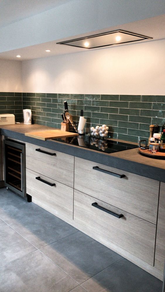 a chic modern kitchen with sleek wooden cabinets, a concrete countertop and a grene tile backsplash