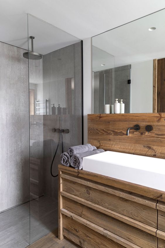 a contemporary chalet bathroom clad with wood and with lots of concrete in decor, with a large mirror, a white sink and a rainshower