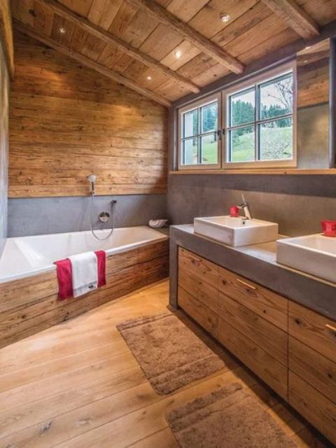 a contemporary chalet bathroom clad with wood, with wooden beams on the ceiling, a large vanity with a concrete countertops and a geometric tub