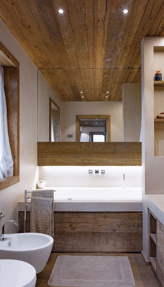 a contemporary chalet bathroom with wood, a tub clad with wood, white appliances and a large mirror plus a built-in vanity