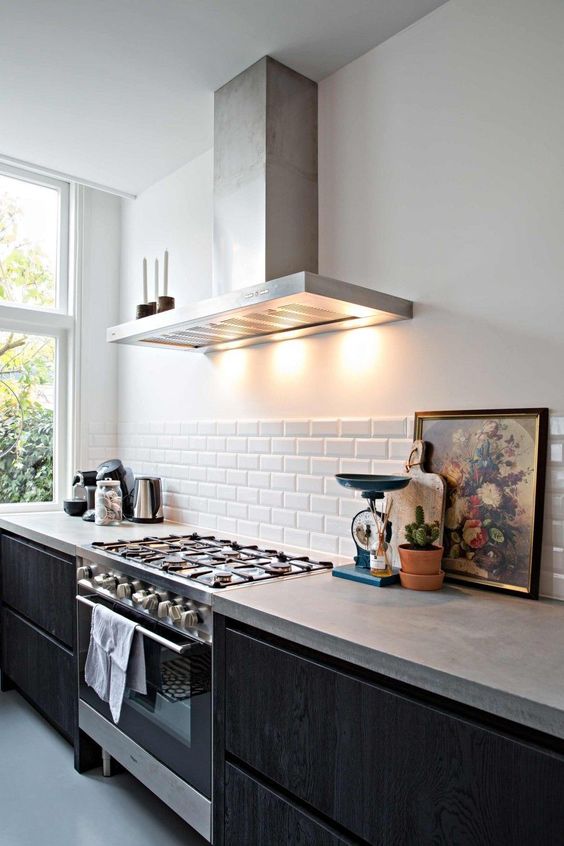 a contemporary kitchen with black cabients, a white subway tile backsplash and concrete countertops