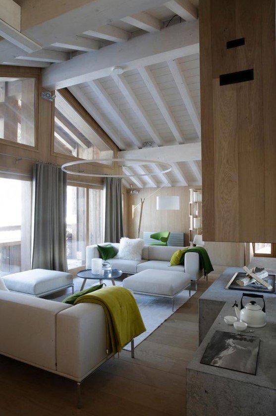 a contemporary light-filled chalet living room with neutral furniture, a glazed wall and an open fireplace of concrete