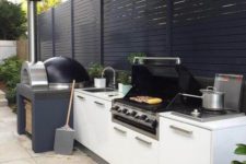 a contemporary outdoor barbecue area done in black and white, with a pizza oven and a grill plus storage cabinets