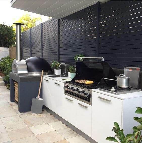 a contemporary outdoor barbecue area done in black and white, with a pizza oven and a grill plus storage cabinets