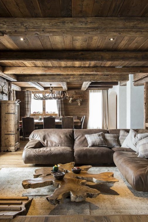 a cozy chalet living room clad with wood, with a large leather sofa, a wood slice table and some antlers