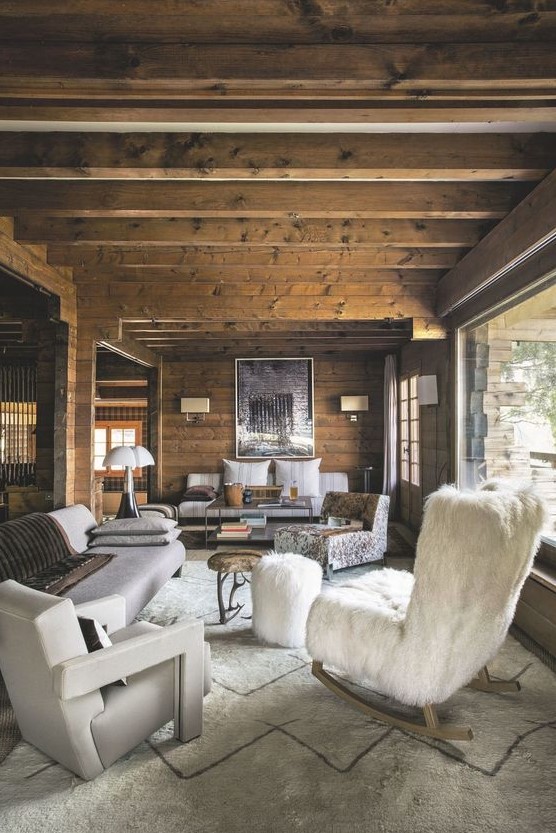 a cozy chalet living room with a wooden ceiling with beams and a glazed wall, stylish and refined furniture and elegant lamps