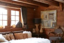 a cozy chalet living space with wooden walls and beams, a grey sofa, a white tile clad table, some art and table lamps