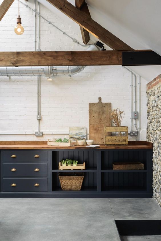 a dark grey kitchen with light stained wooden countertops that match wooden beams and make the space look more refined