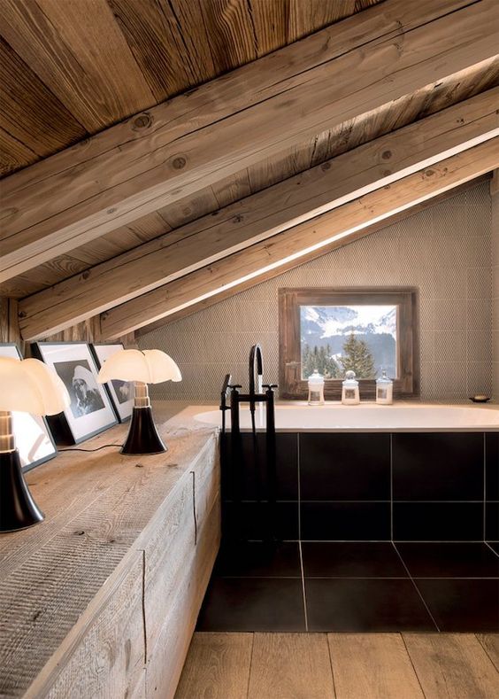 a fab attic chalet bathroom done with whitewashed wood, large scale black tiles, a window for the views and cool lamps