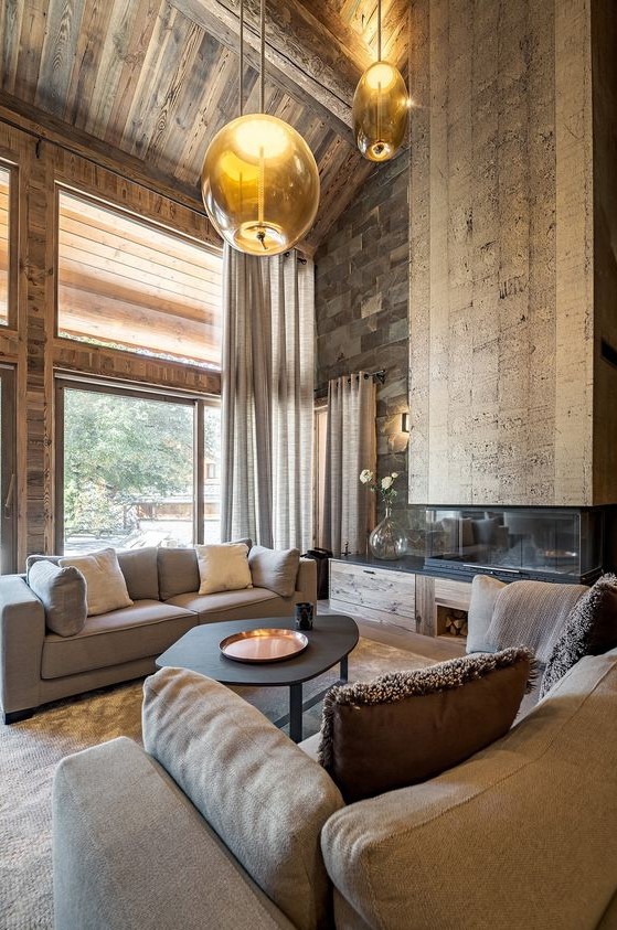 a jaw-dropping chalet living room with all wood around, a stone wall, a catchy fireplace, modern furniture and hanging lamps