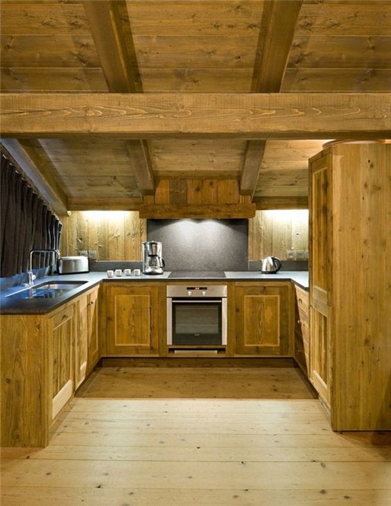 a light-colored chalet kitchen fully done with wood, with a wooden ceiling with beams, built-in lights and stone countertops