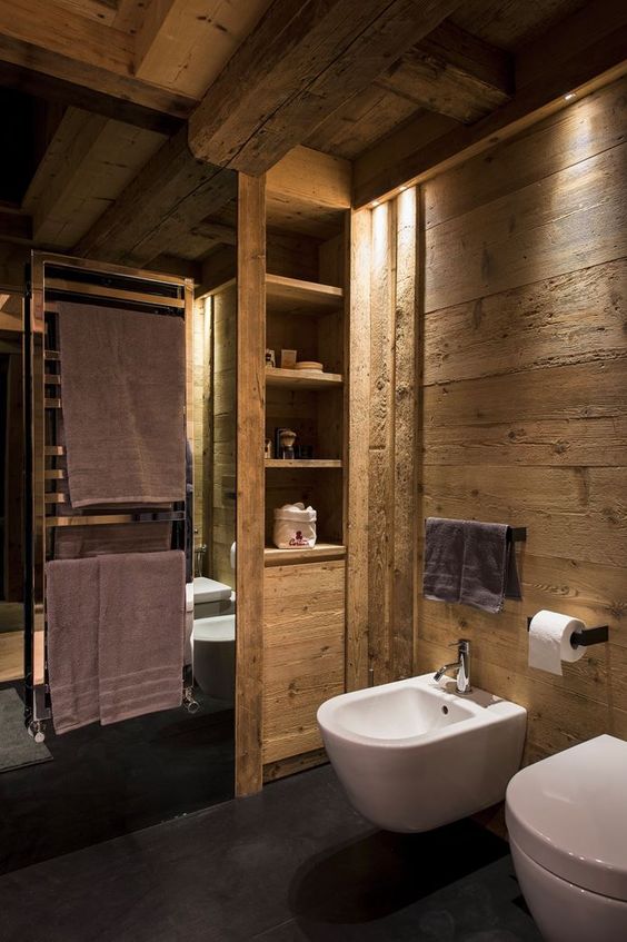 a lovely chalet bathroom clad with textural wood, with white appliances, black holders and built-in lights