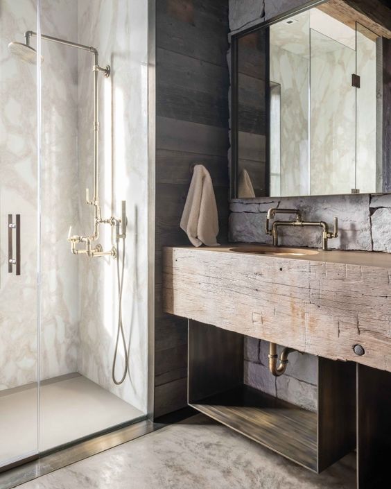 a lovely chalet bathroom done with textural and aged wood, with white stone, antique brass fixtures and a mirror