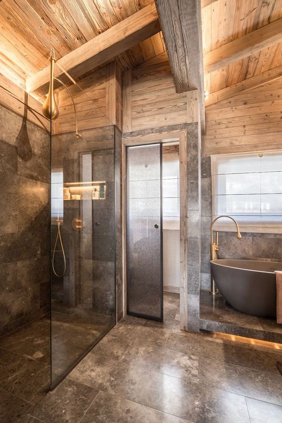 a luxurious chalet bathroom done with grey marble and light-stained wood, with brass touches and a bathtub on a platform