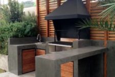 a minimalist bbq area of dark concrete and wood, with a grill and a sink plus a concrete countertop for eating