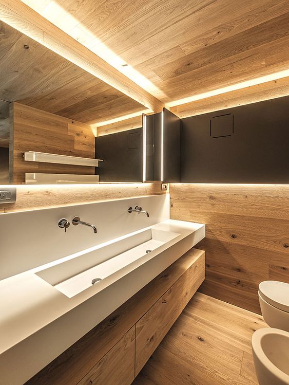 a minimalist chalet bathroom clad with wood, with a sink vanity and an additional wooden one for storage, a large mirror and lights