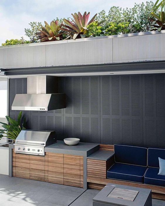 a minimalist outdoor bbq area of concrete, wood and metal with a cooking zone, a grill with a hood and a sitting zone