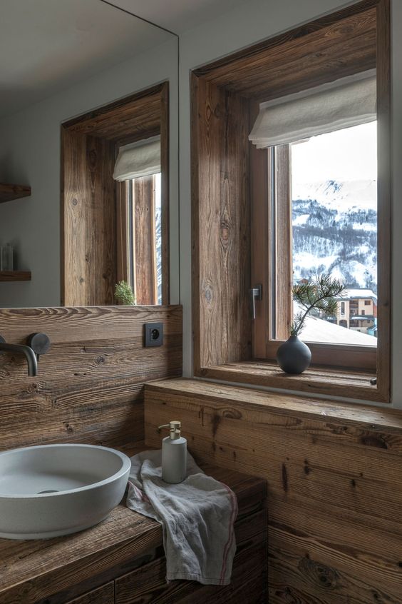 a modern bathroom clad with wood, with a window for the views, a stone sink and modern fixtures looks chic and cool