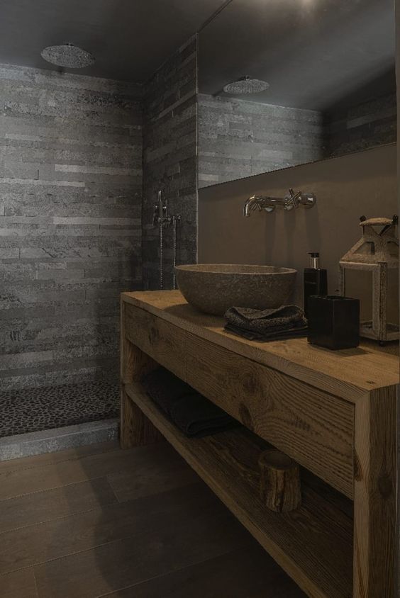 a modern chalet bathroom done with wood, stone tiles and pebbles in the shower, with a stone sink and a large mirror