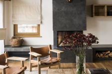 a modern chalet living room with a wooden ceiling, leather chairs and a wooden table plus a concrete fireplace with a storage compartment