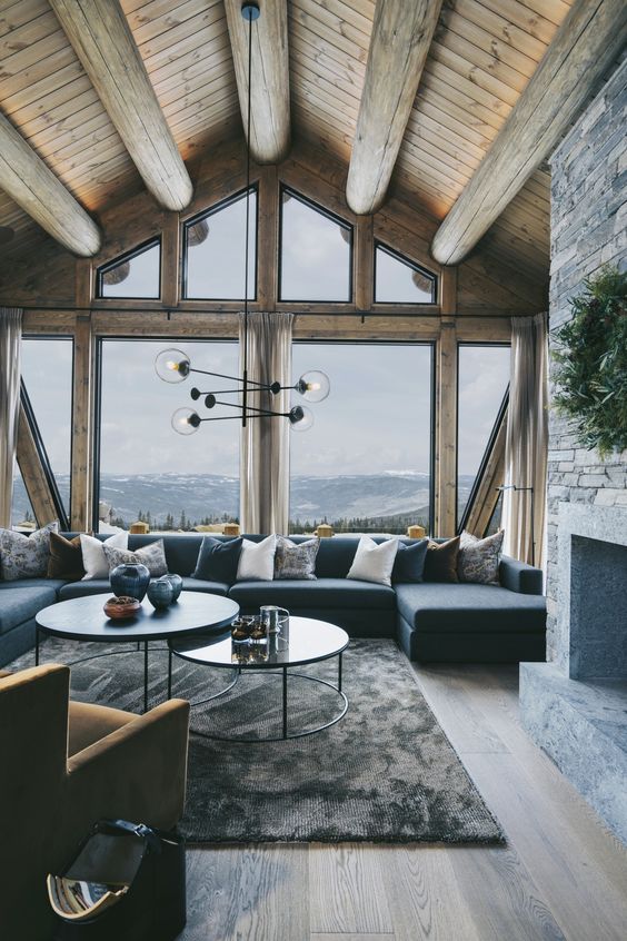 a modern chalet living room with stained wooden beams and a ceiling, a large navy sectional , round tables and a fireplace