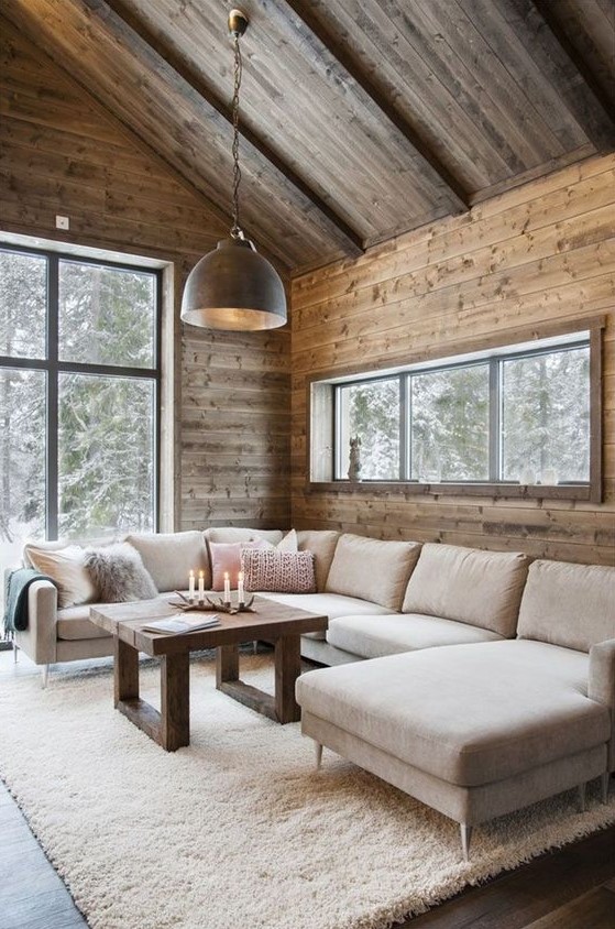 a modern chalet living room with wooden walls and a ceiling, a neutral sectional, a metal pendant lamp