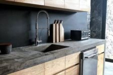 a moody kitchen with sleek wooden cabinets, a chalkboard backsplash and a concrete countertop