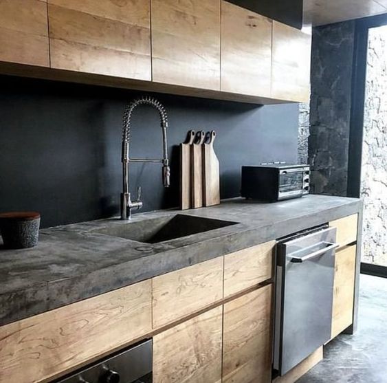 a moody kitchen with sleek wooden cabinets, a chalkboard backsplash and a concrete countertop