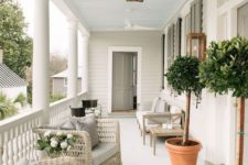 a neutral summer porch with creamy wicker and wooden furniture, potted greenery and comfy chairs in brown