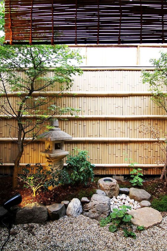 un jardín japonés tranquilo con rocas y guijarros, una linterna de piedra, dos árboles, vegetación y luces es muy elegante