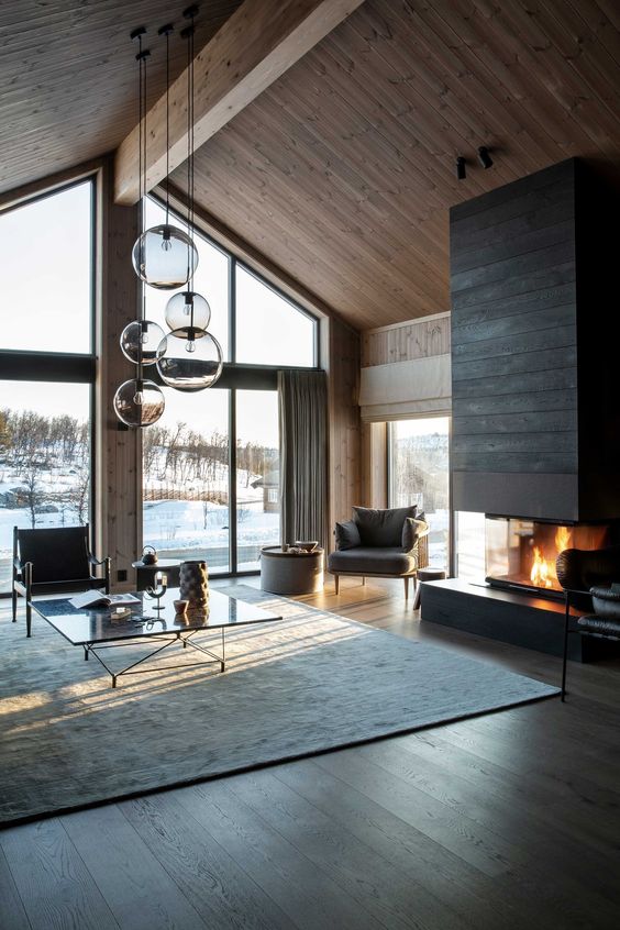 a peaceful Scandi-inspired chalet living room with wooden walls and a ceiling, a dark wood clad fireplace, a chic coffee table and chairs