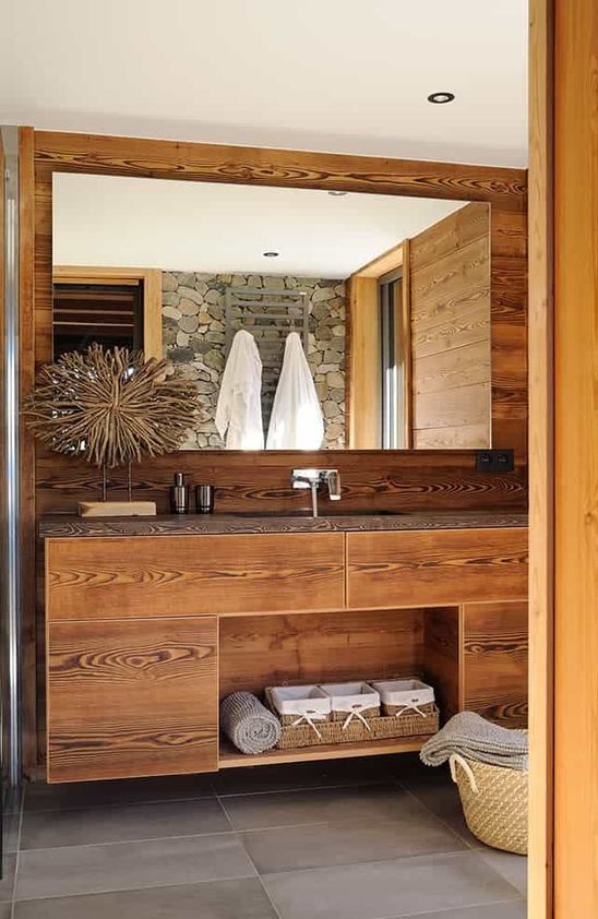 a pretty chalet bathroom clad with wood, with a built-in vanity, a large mirror, a basket for storage and a pretty artwork