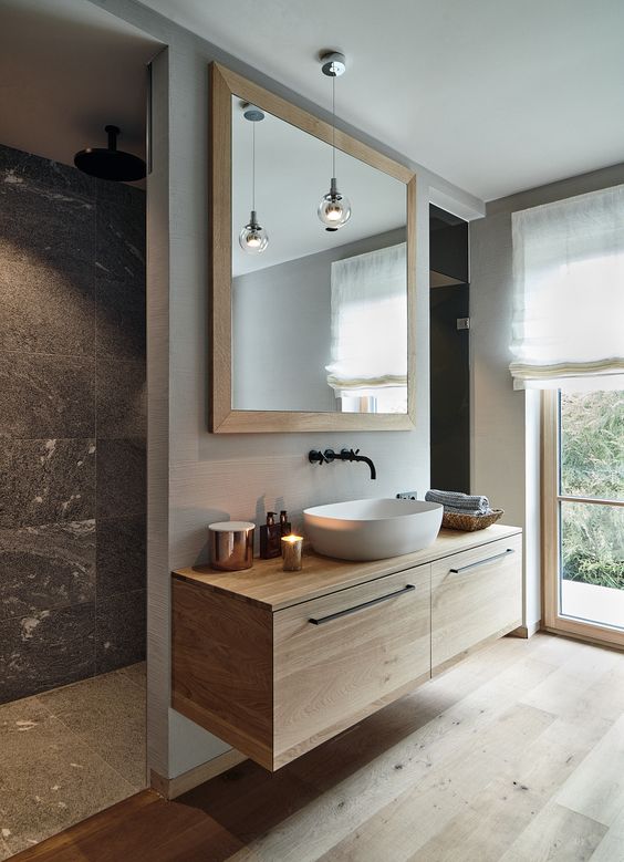 a pretty modern chalet bathroom done with blonde wood, grey stone tiles, a floating vanity, a chic sink and a large mirror