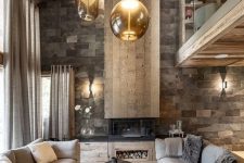 a refined chalet living room with a stone wall, a fireplace, a wooden ceiling, grey sofas and hanging glass lamps