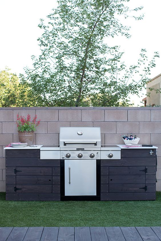 a rustic outdoor bbq area of dark stained wood, with a large grill and some cooking space