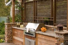 a rustic outdoor bbq zone built of wood and stone, with a cooking countertop and a grill plus lanterns around