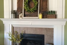 a rustic summer mantel with a greenery wreath, greenery in a planter, a yellow jar, a churn and a pallet wood piece