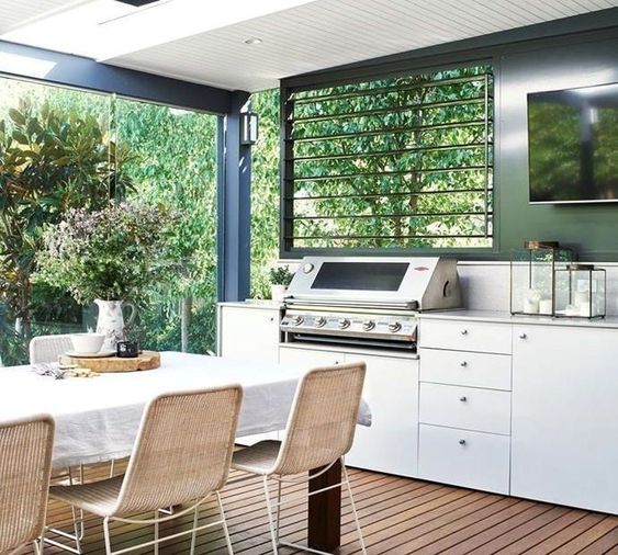 a simple modern outdoor dining space with a white table and rattan chairs plus a grill