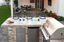 a simple rustic bbq area built of stone, with storage units and a grill plus an eating zone