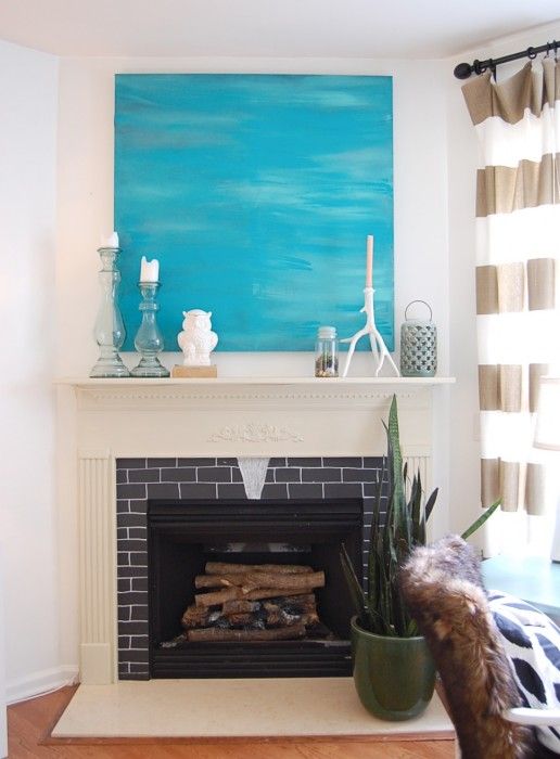 a simple summer mantel with a turquoise artwork, candles in glass candle holders and a candle lantern