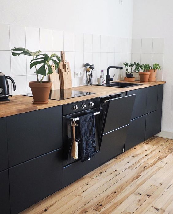 a sleek matte black kitchen with light stained wooden countertops and a white tile backsplash for a contrast